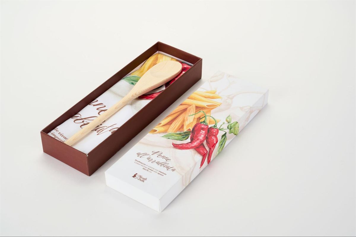 An open kitchen gift set with a cotton towel and a wooden spoon inside a brown box